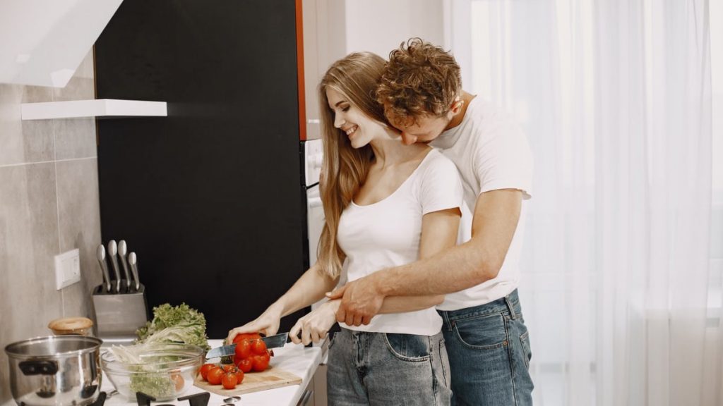 Happy couple preparing a meal together in a bright, modern kitchen, embracing and smiling.